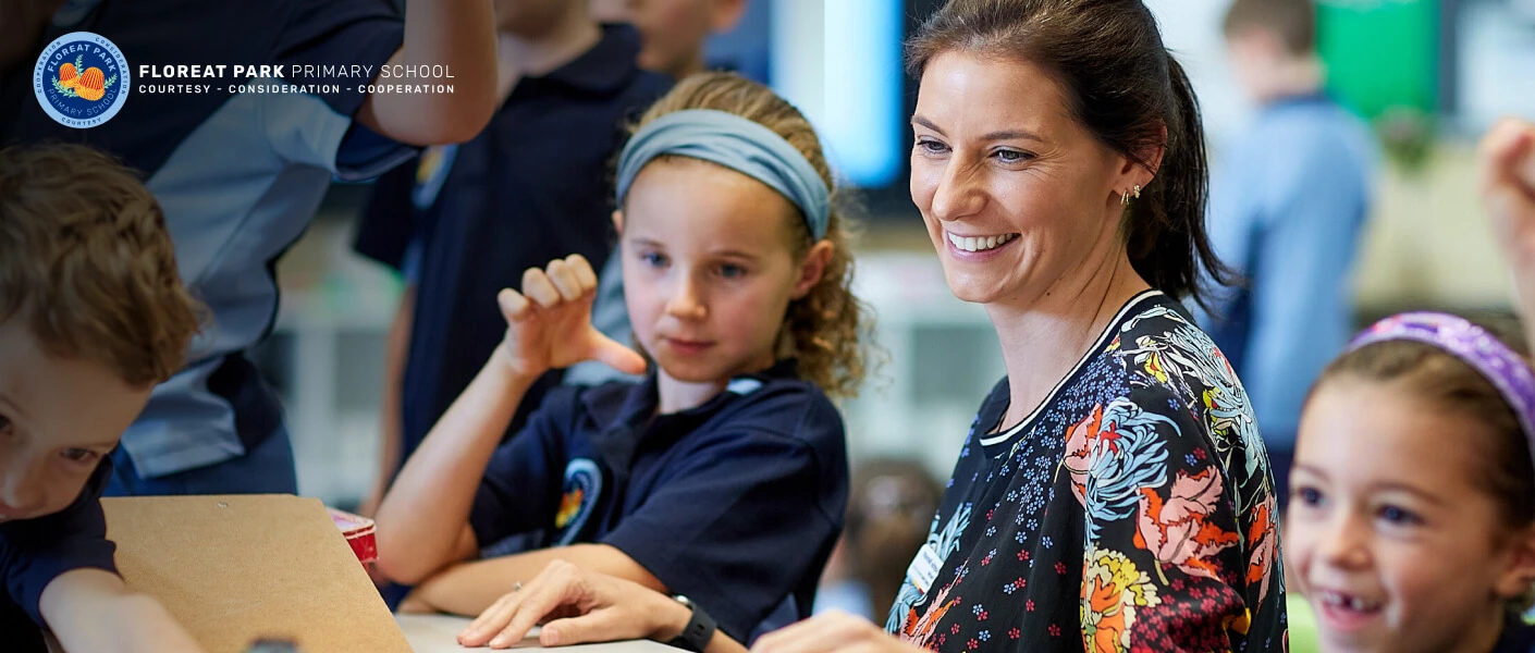 Teacher smiling alongside engaged primary school students working on laptops, representing modern and community-focused education website design for a primary school.